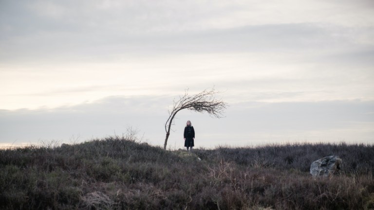 A hillside with a creepy tree and a woman standing alone in Doctor Who episode "73 Yards"