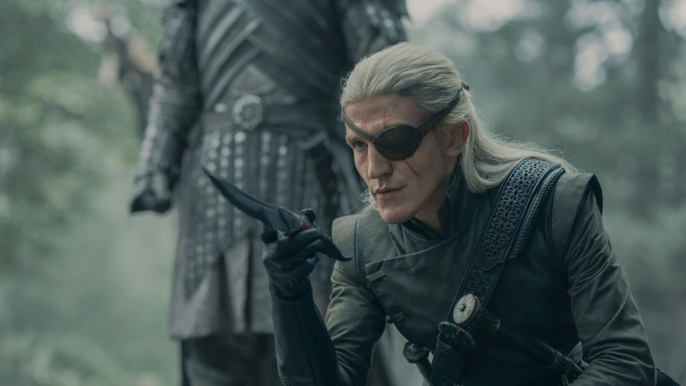 Aemond Targaryen (Ewan Mitchell) sits pointing a dagger toward an unseen object or person