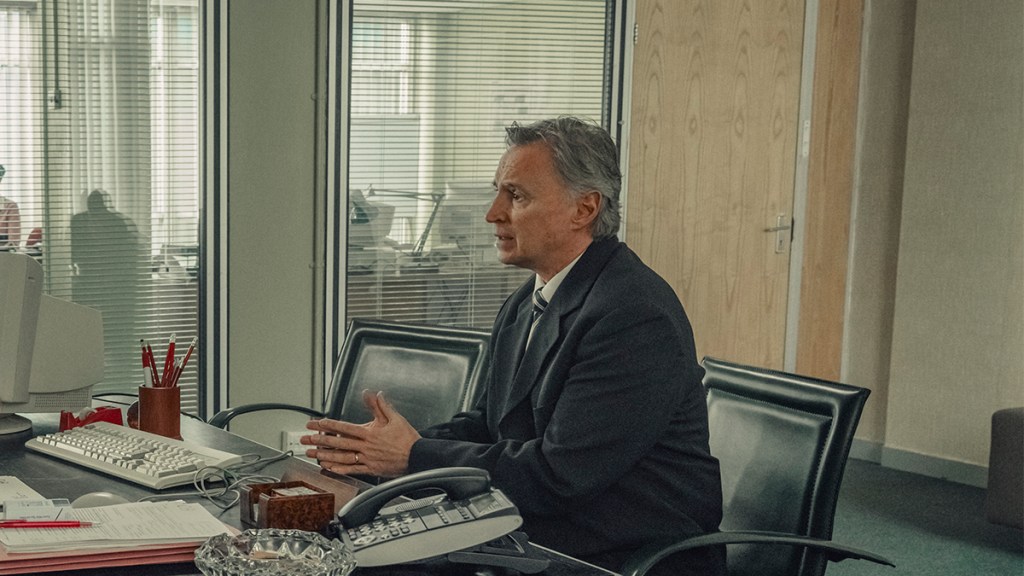 A man in a suit sitting at an office desk in Netflix's Toxic Town