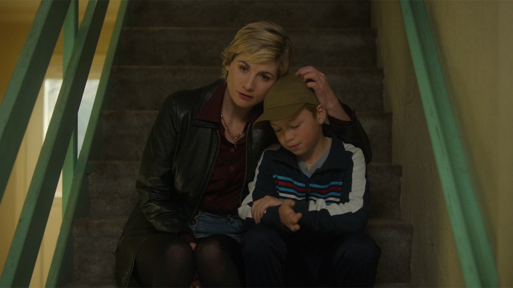 A woman with short blonde hair sitting on the stairs with a young boy wearing a cap