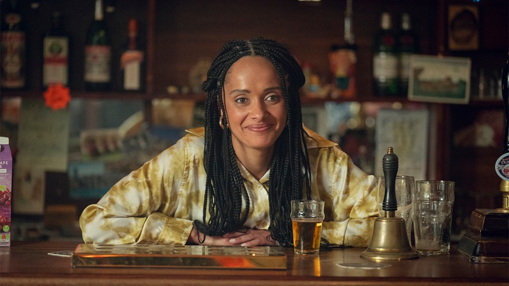 A woman with long braids behind the bar of a pub in Netflix's Toxic Town